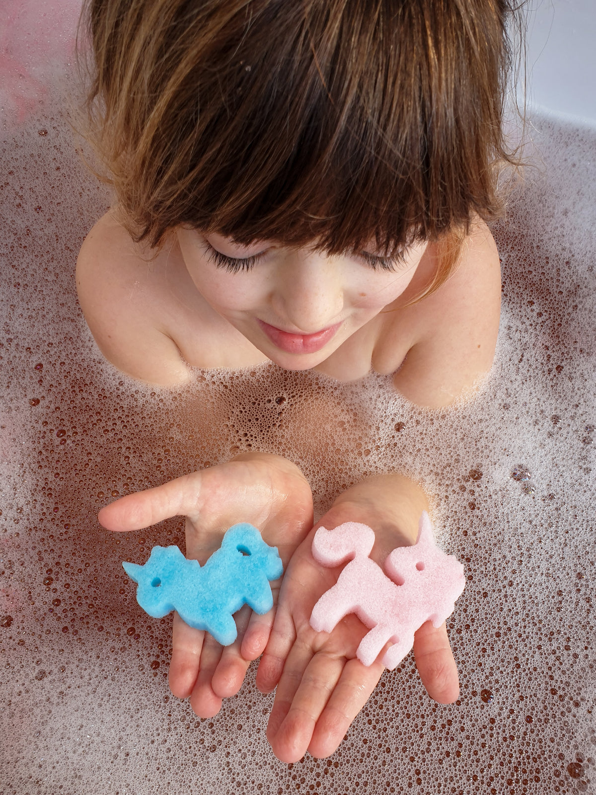 Girl in a bubble bath holding unicorn sponge toys