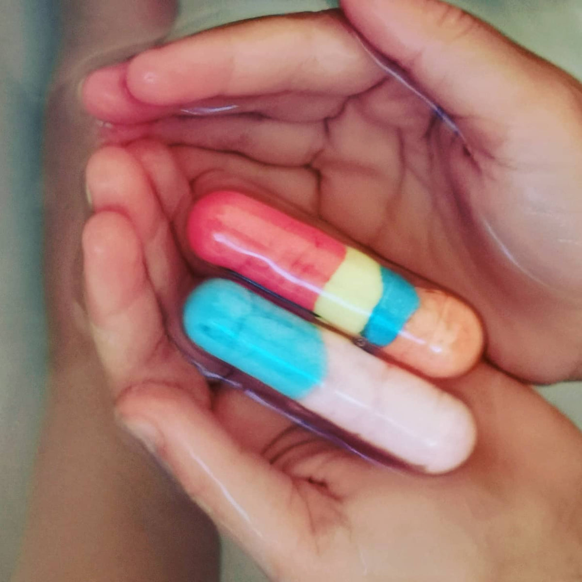 Hands holding pink, white and blue Bath Beans capsules