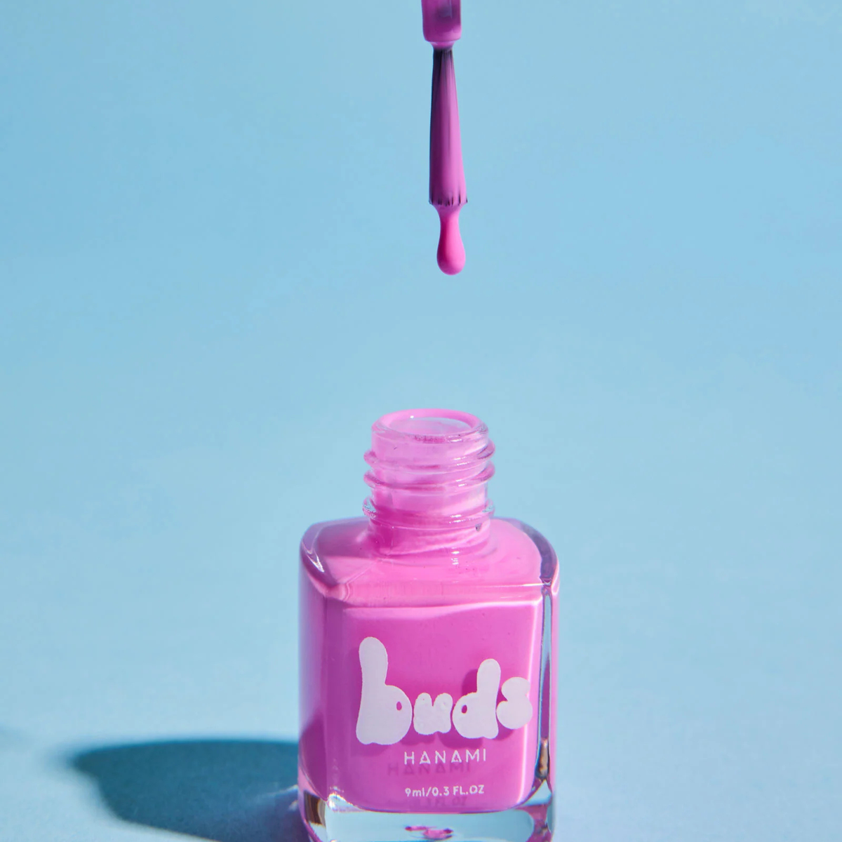 Pink Buds kids nail polish dripping from the brush into the bottle on a blue background