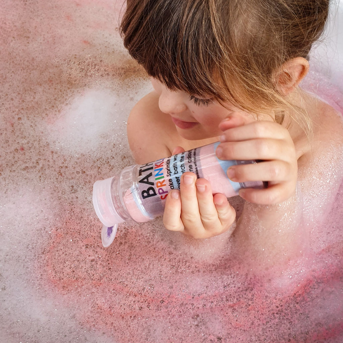 Child holding a Bath Sprinkles shaker over purple bubbly bath water