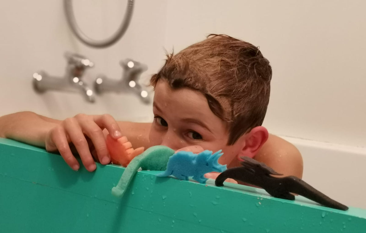Boy in the bath playing with dinosaur sponge toys