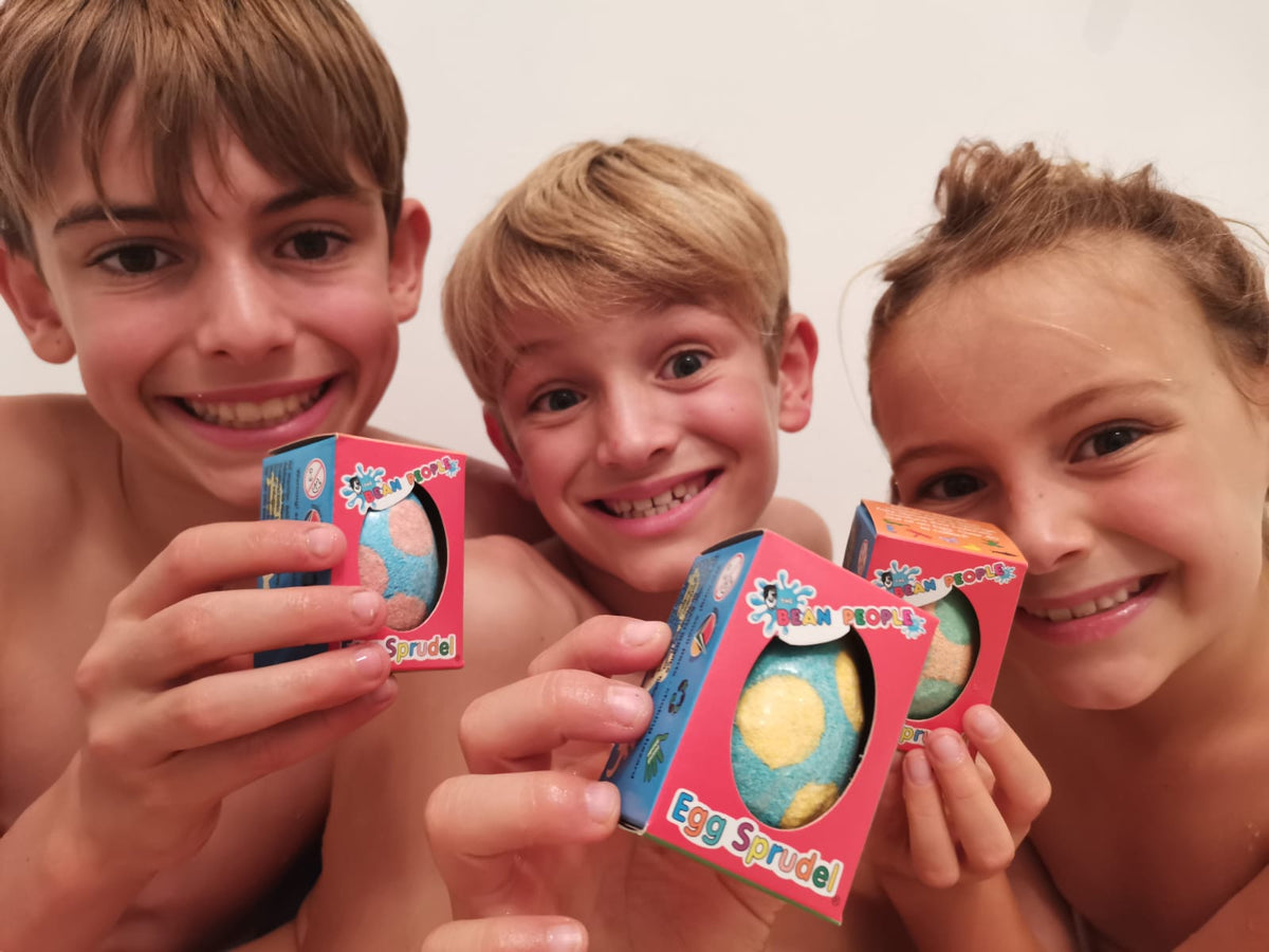 Three smiling kids holding boxed Egg Bath Bomb Sprudels in the bath