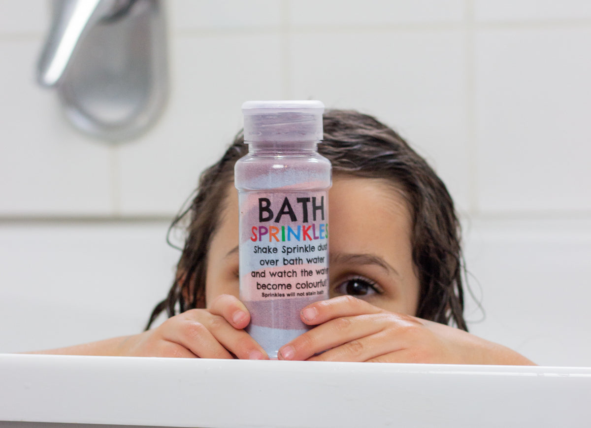 Girl in the bath with a purple Bath Sprinkles shaker