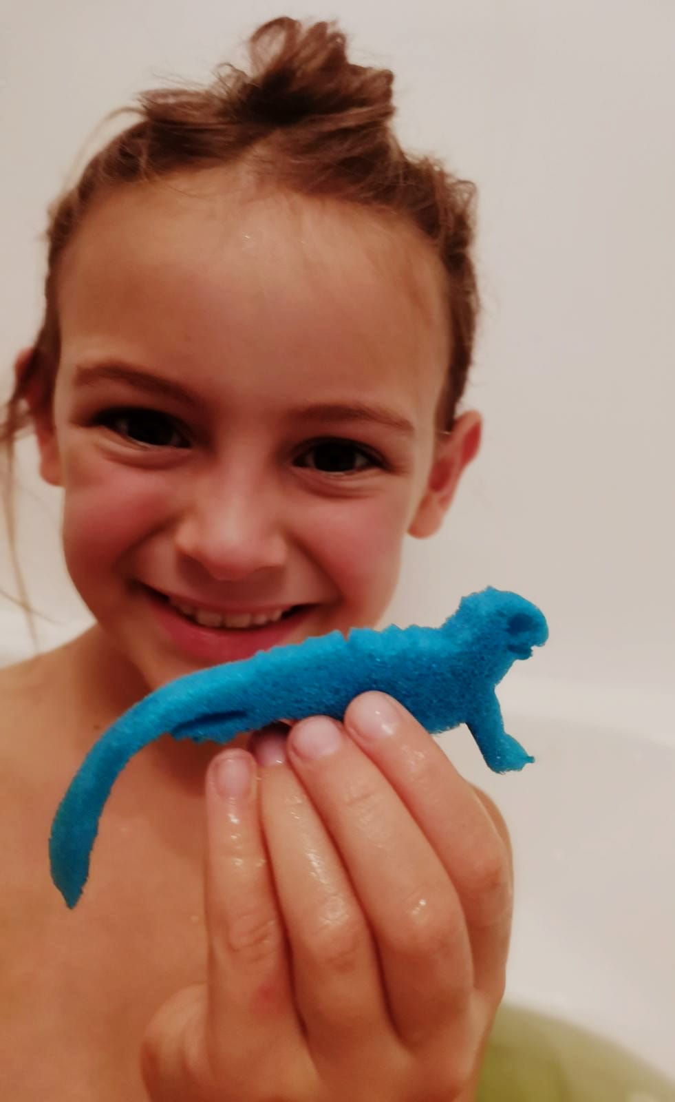 Smiling girl holding a blue lizard sponge toy from an Egg Bath Bomb Sprudel