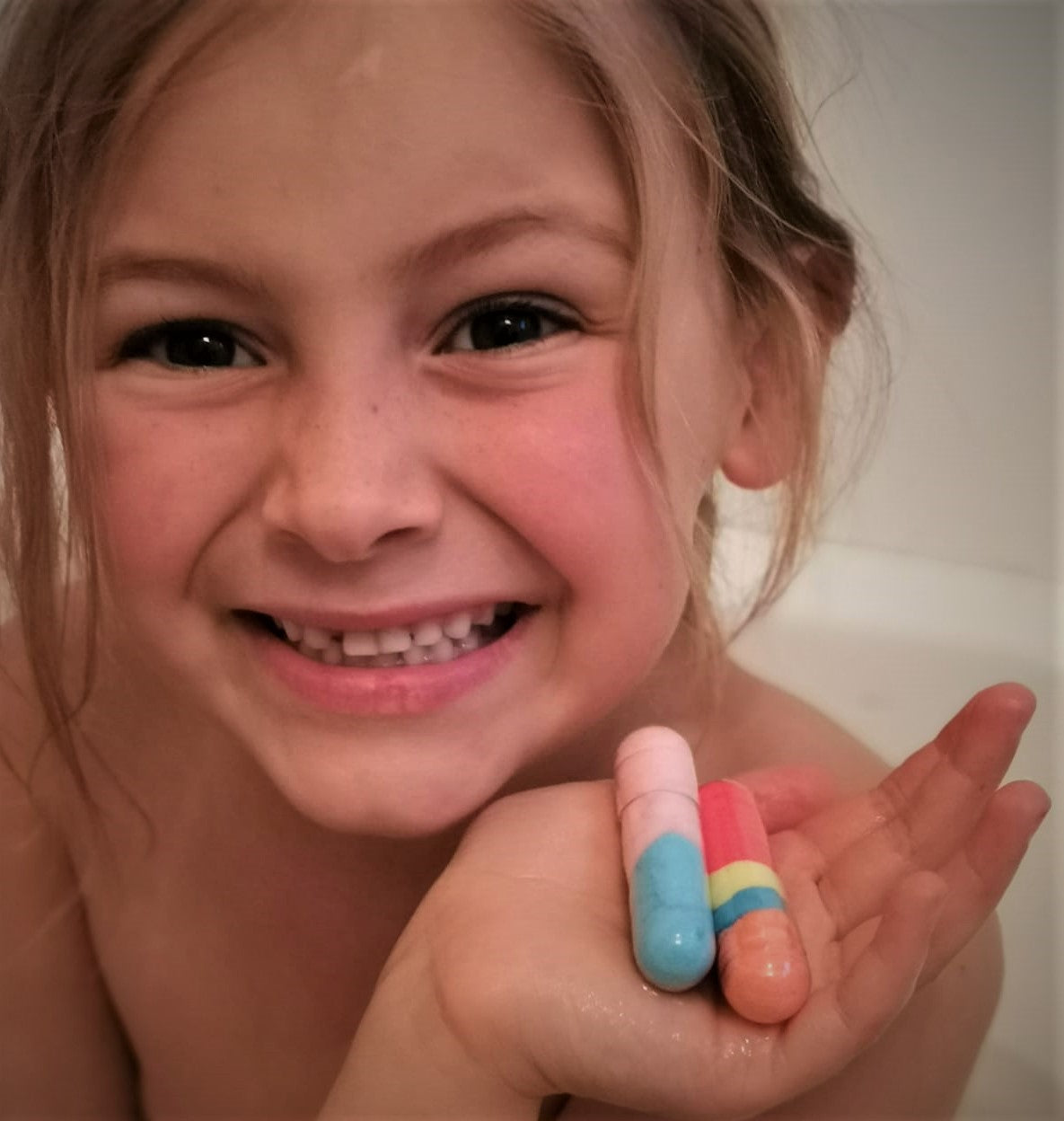 Smiling girl in the bath holding Bath Beans capsules