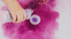 childs hand shaking purple bath sprinkles into water